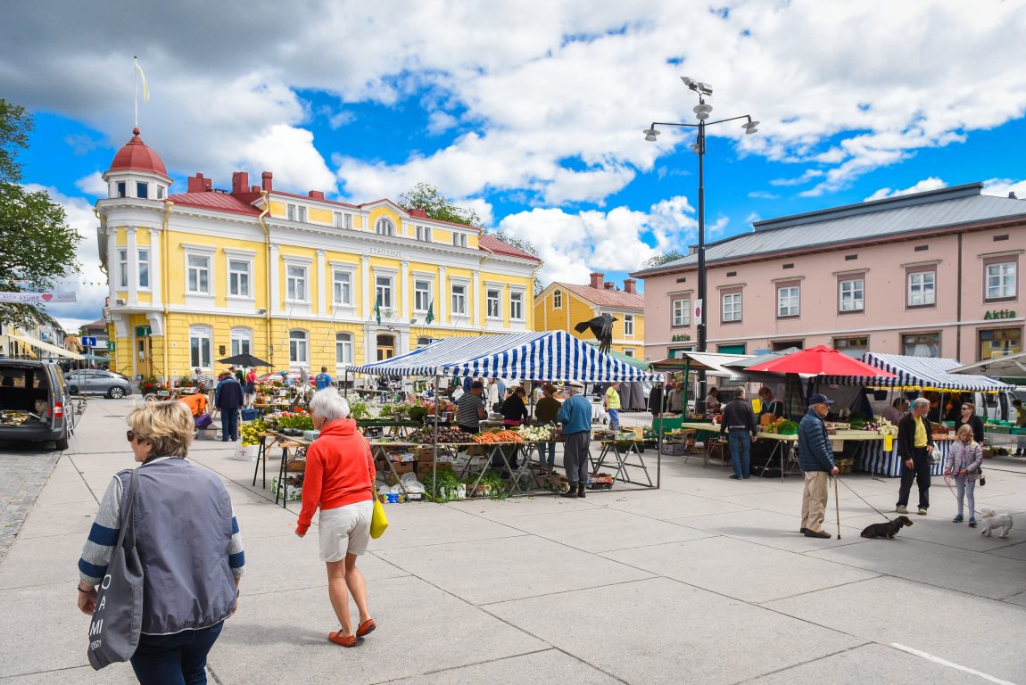 Människor går på Ekenäs torg. Gamla stadshuset syns i bakgrunden.